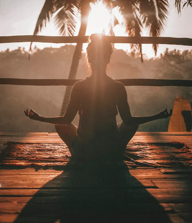 A silhouette of a person meditating outdoors at sunrise representing daily habits for healthy living and wellness