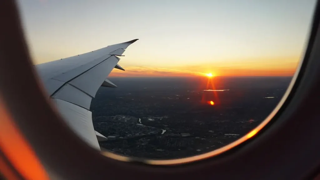 Airplane wing and sunset view from a passenger window over a city.