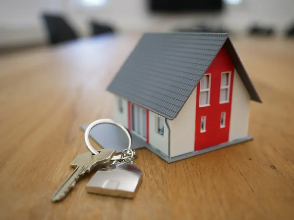 Small model house and silver key on a wooden table.