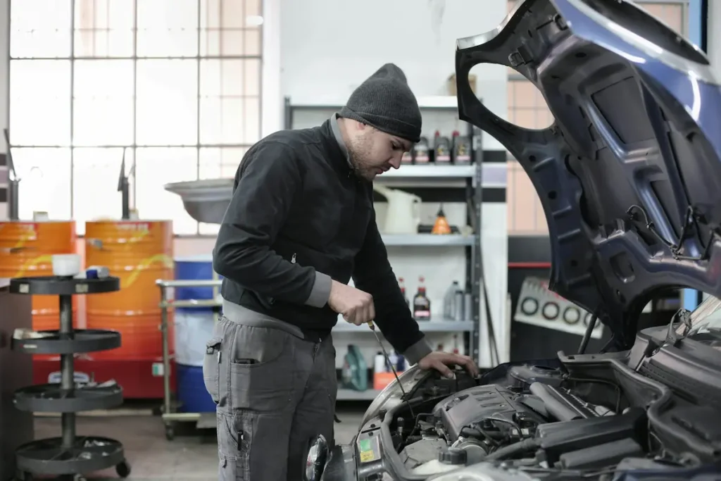 A mechanic inspecting the engine under the hood of a car in an auto repair shop.