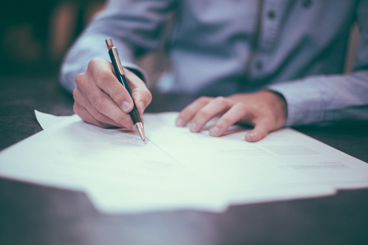 Business professional signing financial documents with a pen, contract papers and calculator on wooden desk