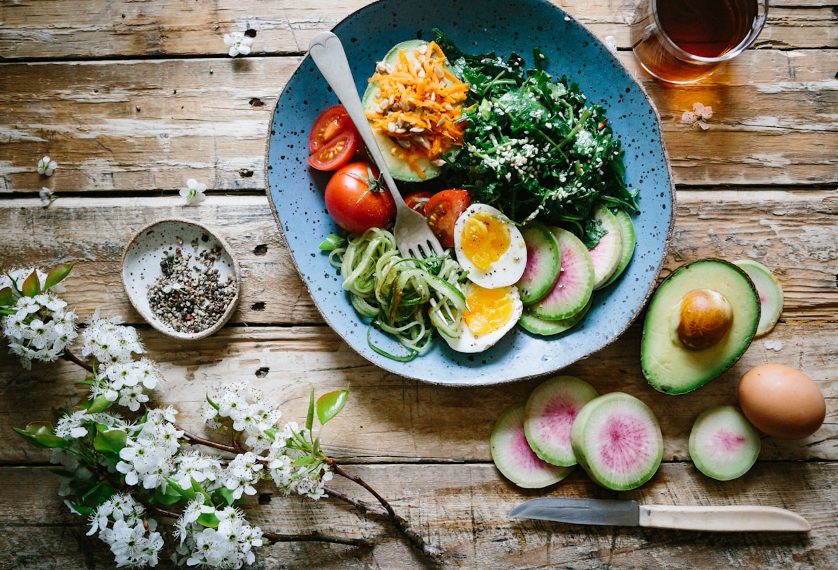 Colorful array of whole foods including vegetables, fruits, grains, and proteins arranged on a wooden table