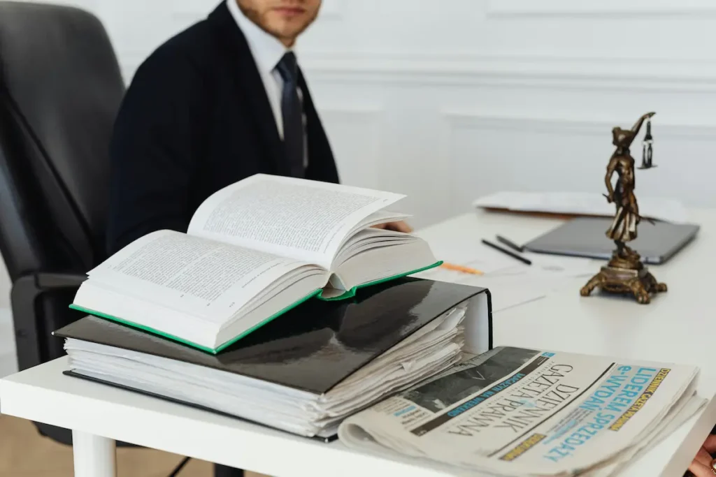 Open law book and scales of justice on a desk with a corporate attorney in the background.