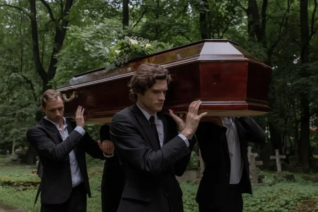 A group of pallbearers in black suits carrying a wooden coffin during a funeral service.
